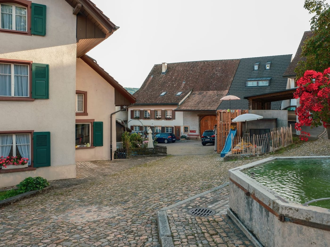 Dorfplatz mit Brunnen und alten Bäumen