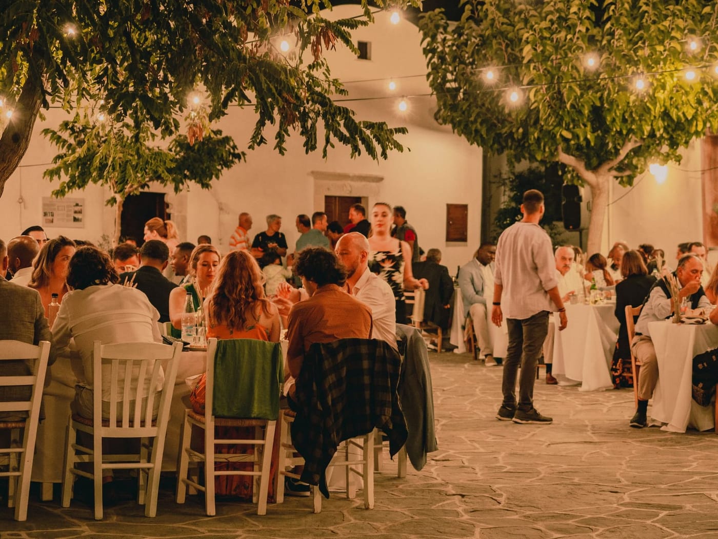 Menschen sitzen abends unter Lichterketten zusammen